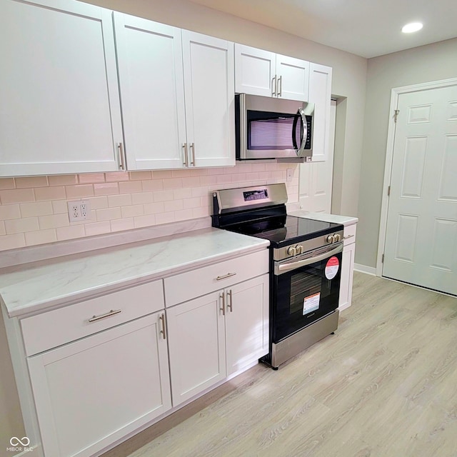 kitchen with white cabinetry, light stone counters, light wood-type flooring, appliances with stainless steel finishes, and decorative backsplash