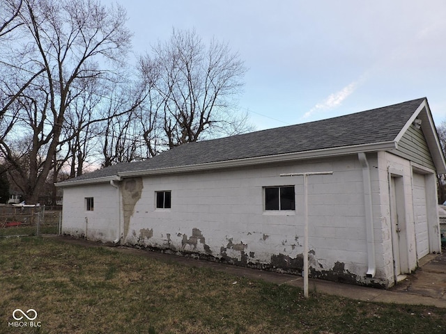 view of home's exterior with roof with shingles, concrete block siding, and fence