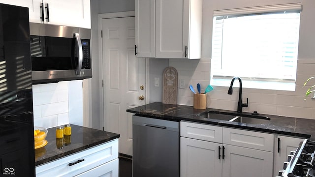 kitchen with white cabinetry, appliances with stainless steel finishes, backsplash, dark stone countertops, and sink