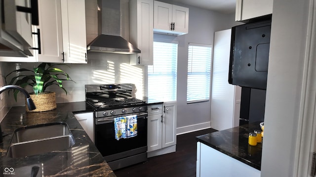 kitchen featuring white cabinetry, stainless steel range with gas cooktop, dark stone countertops, wall chimney range hood, and sink