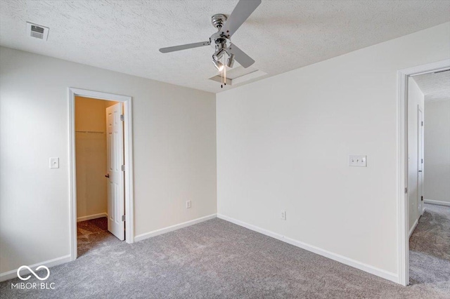 unfurnished bedroom with ceiling fan, a textured ceiling, light carpet, a spacious closet, and a closet