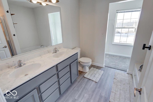 bathroom featuring wood-type flooring, a bath, vanity, and toilet