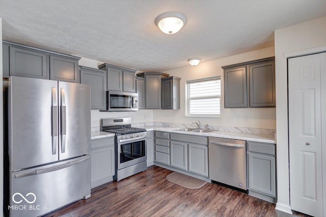 kitchen with sink, a textured ceiling, dark hardwood / wood-style floors, gray cabinets, and stainless steel appliances