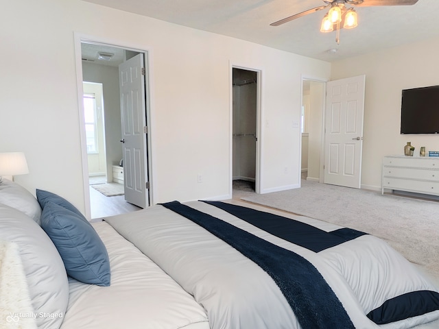 bedroom featuring a walk in closet, light colored carpet, ceiling fan, ensuite bath, and a closet