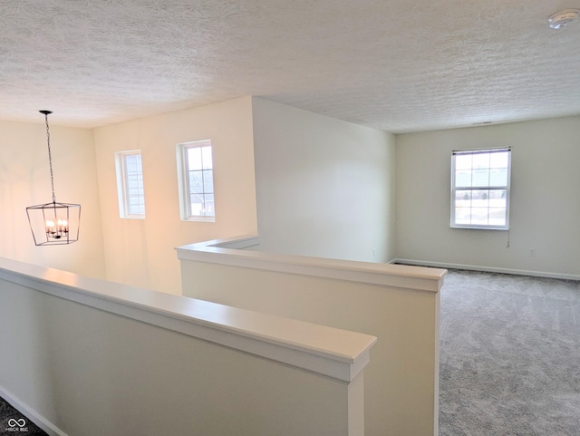 hallway with a chandelier, a textured ceiling, carpet, and a wealth of natural light