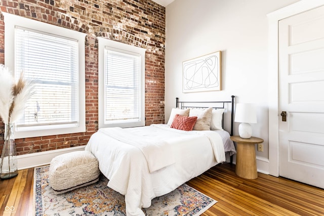 bedroom featuring brick wall and hardwood / wood-style flooring