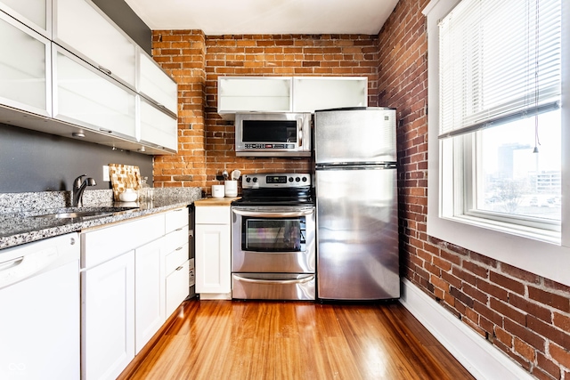 kitchen with brick wall, appliances with stainless steel finishes, white cabinets, and light stone countertops