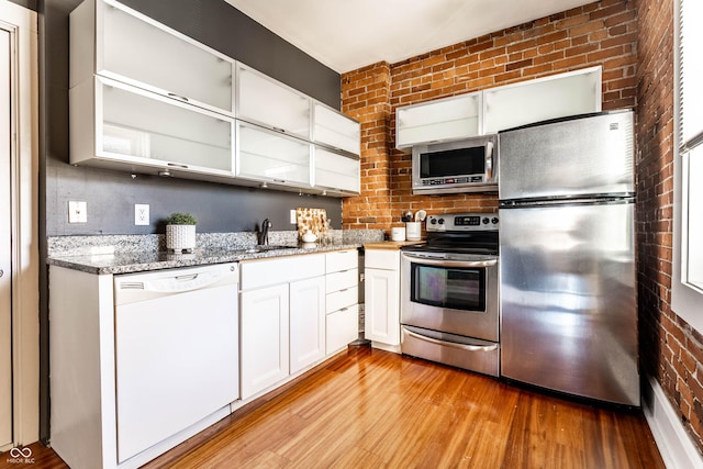 kitchen featuring white cabinetry, light hardwood / wood-style floors, appliances with stainless steel finishes, brick wall, and sink