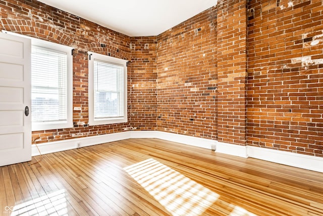 empty room with brick wall and hardwood / wood-style floors