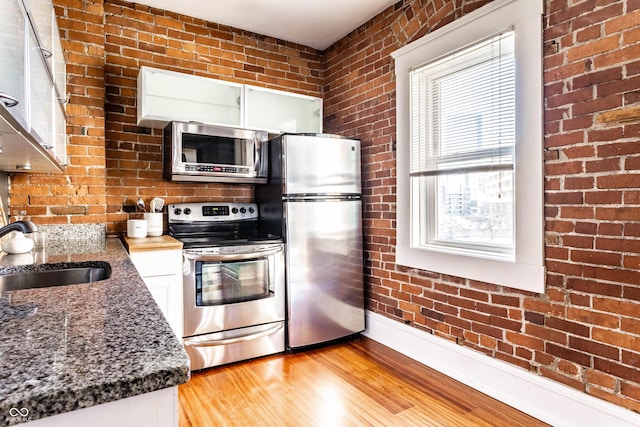 kitchen with sink, white cabinetry, light hardwood / wood-style flooring, appliances with stainless steel finishes, and brick wall