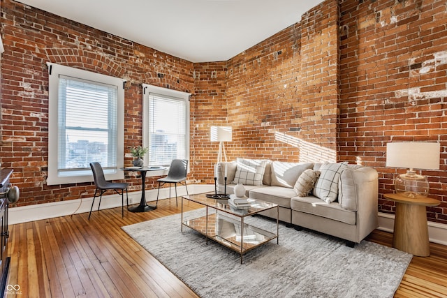 living room with hardwood / wood-style flooring, baseboards, and brick wall