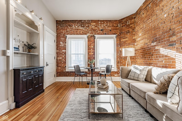 living room with brick wall, baseboards, and light wood-style floors