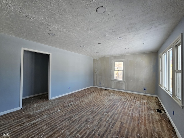 spare room featuring a textured ceiling, dark hardwood / wood-style flooring, and a healthy amount of sunlight