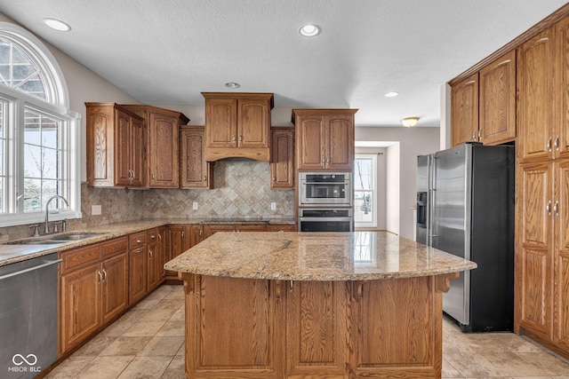 kitchen with a kitchen island, stainless steel appliances, sink, backsplash, and light stone counters