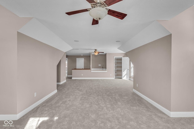 unfurnished living room featuring ceiling fan, built in shelves, vaulted ceiling, and carpet