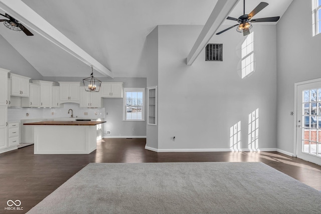 unfurnished living room featuring ceiling fan, sink, a towering ceiling, and beamed ceiling