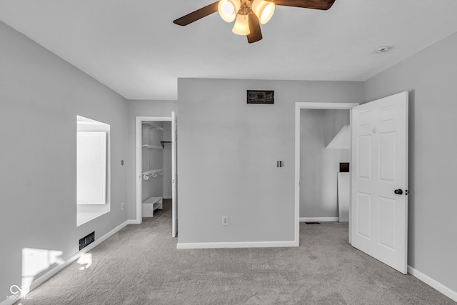 unfurnished bedroom featuring ceiling fan, a walk in closet, a closet, and light colored carpet