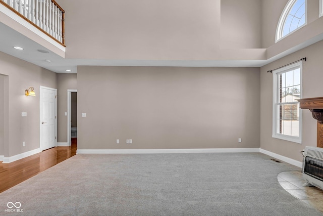 interior space with heating unit, light colored carpet, a high ceiling, and a wood stove