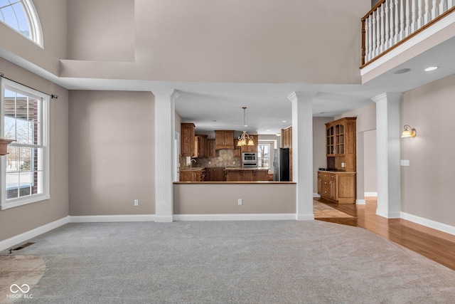 unfurnished living room with light carpet, a high ceiling, and decorative columns