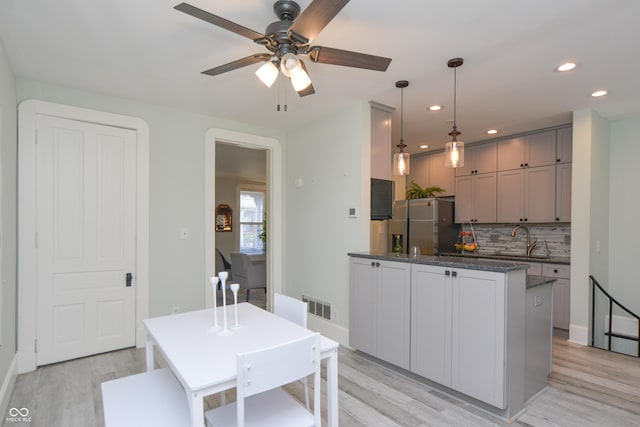 kitchen featuring pendant lighting, decorative backsplash, stainless steel fridge with ice dispenser, ceiling fan, and light hardwood / wood-style flooring