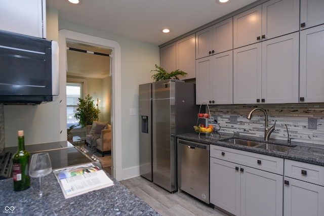 kitchen with dark stone countertops, decorative backsplash, sink, light hardwood / wood-style flooring, and stainless steel appliances