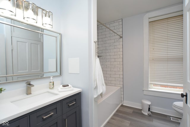 full bathroom featuring hardwood / wood-style flooring, tiled shower / bath combo, vanity, and toilet