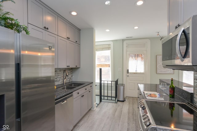 kitchen featuring appliances with stainless steel finishes, dark stone counters, sink, gray cabinets, and light hardwood / wood-style flooring