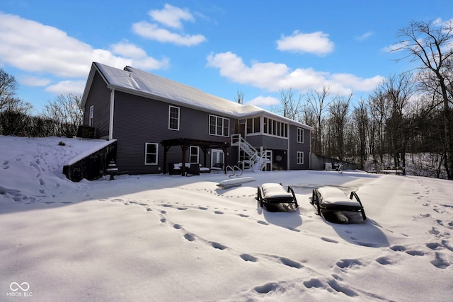 snow covered back of property featuring a sunroom