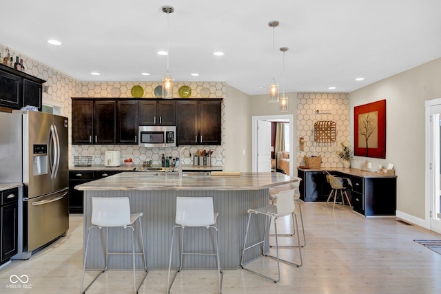 kitchen featuring decorative light fixtures, a kitchen island with sink, stainless steel appliances, and a kitchen bar