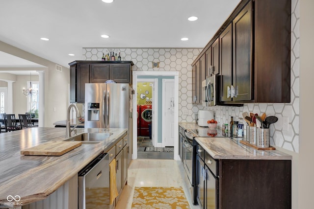 kitchen featuring washer / dryer, appliances with stainless steel finishes, a notable chandelier, dark brown cabinets, and sink