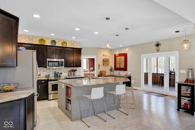 kitchen featuring a center island with sink, pendant lighting, dark brown cabinetry, stainless steel appliances, and light stone counters