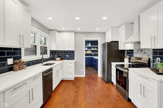 kitchen with wood-type flooring, sink, stainless steel appliances, white cabinets, and wall chimney exhaust hood