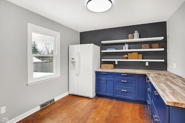 kitchen featuring hardwood / wood-style floors, white refrigerator with ice dispenser, butcher block counters, and blue cabinets