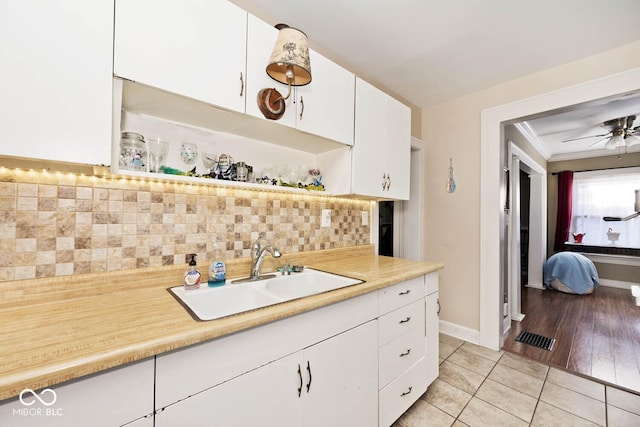 kitchen with light tile patterned floors, ceiling fan, decorative backsplash, white cabinets, and sink