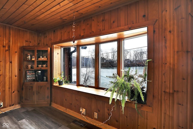 interior space with dark hardwood / wood-style flooring, wooden walls, wooden ceiling, and a water view