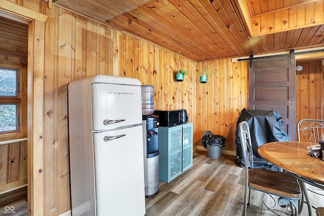 kitchen featuring white refrigerator, wooden walls, wood ceiling, and a barn door