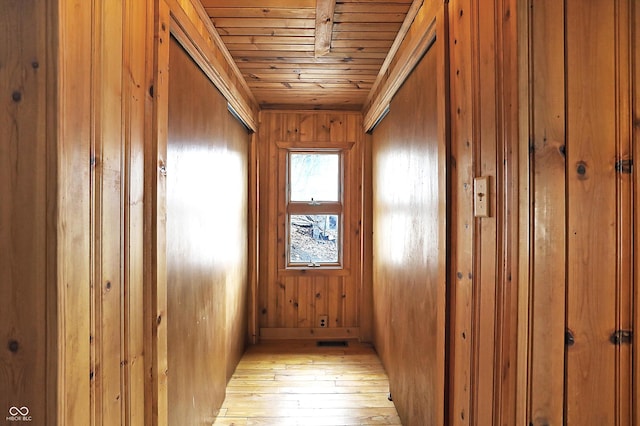 hall with light hardwood / wood-style flooring, wooden ceiling, and wood walls