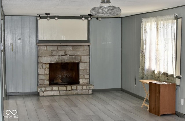 unfurnished living room featuring a textured ceiling, a stone fireplace, light hardwood / wood-style floors, and wooden walls