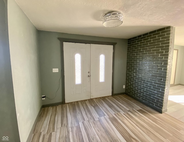 foyer entrance featuring brick wall, a textured ceiling, and light wood-type flooring