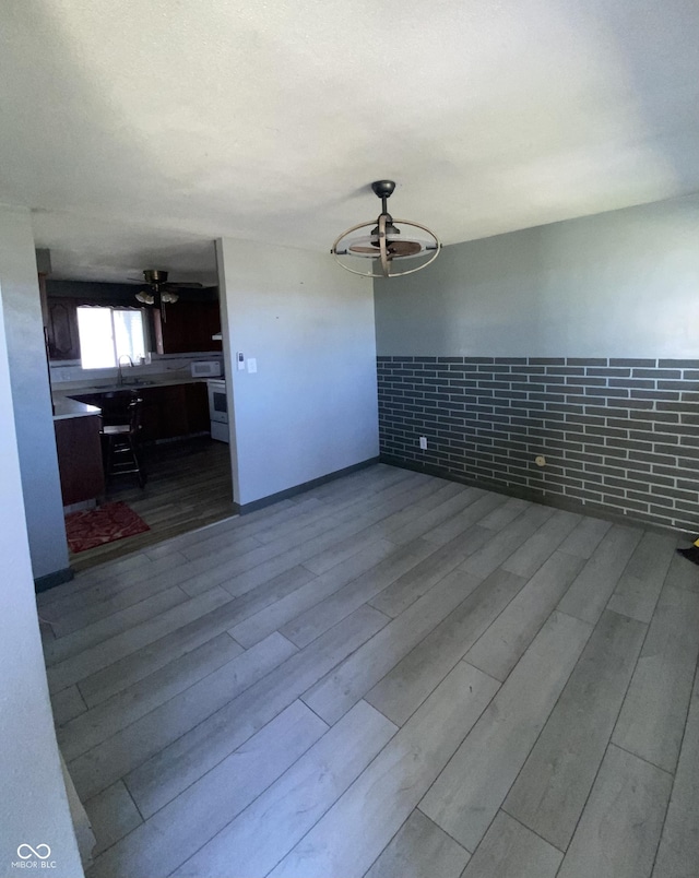 empty room with ceiling fan, brick wall, and light hardwood / wood-style floors