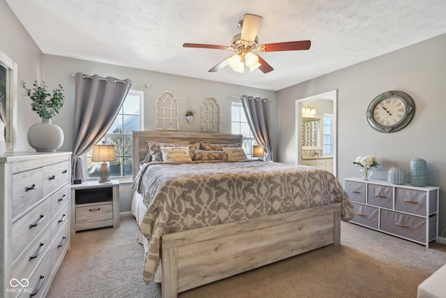 bedroom with ceiling fan, connected bathroom, light carpet, and a textured ceiling