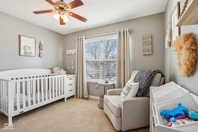 bedroom with a nursery area, light colored carpet, and ceiling fan