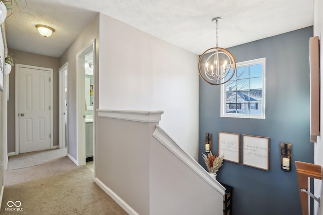 hallway featuring light colored carpet, a chandelier, and a textured ceiling