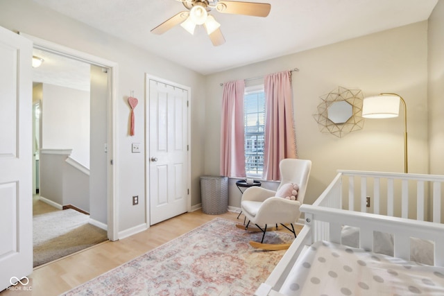 bedroom with a crib, ceiling fan, and light hardwood / wood-style floors