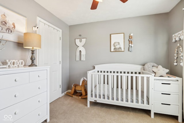 bedroom featuring a nursery area, ceiling fan, and light carpet