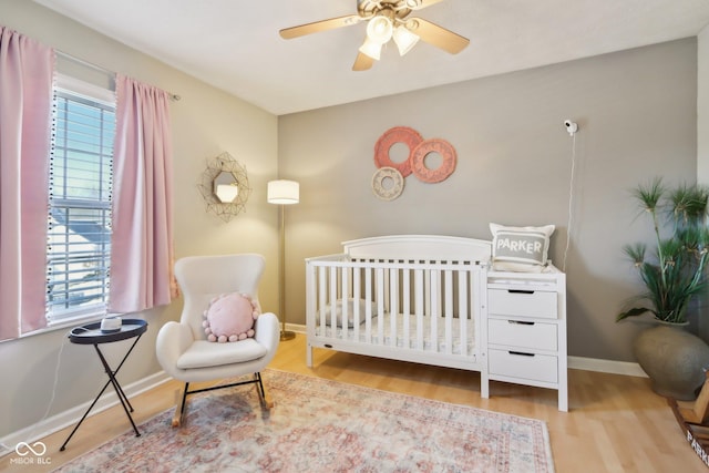 bedroom featuring a crib, light hardwood / wood-style floors, and ceiling fan