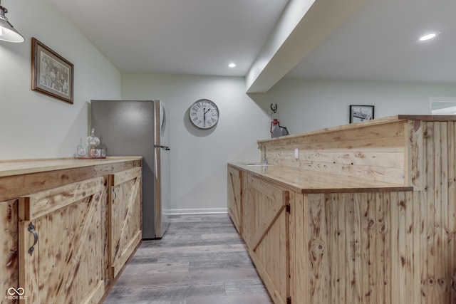 bar featuring sink, wood-type flooring, stainless steel fridge, and light brown cabinets