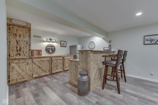 bar with stainless steel fridge, light brown cabinets, and light hardwood / wood-style flooring