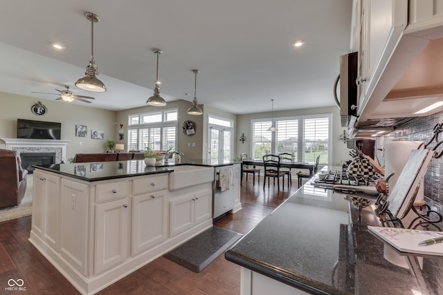 kitchen with white cabinetry, stainless steel appliances, decorative light fixtures, and a kitchen island with sink