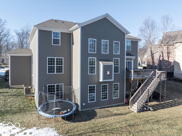 rear view of house with a trampoline, a wooden deck, a yard, and central air condition unit